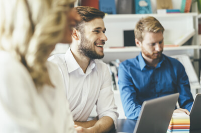 Person with a laptop smiling while surrounded by others in a meeting